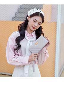 Close-up of light grey quilted leather wallet with gold metal trim and wrist strap