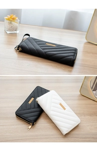 Close-up of quilted long wallets in black and white with gold hardware on wooden surface