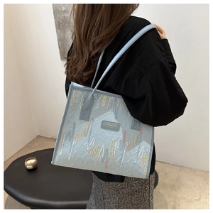 Detailed view of light blue tote bag with colorful embroidery on a model's shoulder