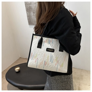 Detailed side view of white tote bag with colorful wave embroidery and black trim accents