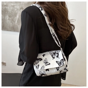 Close-up of white crossbody bag featuring black butterfly patterns and a wide strap