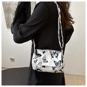 Detail view of white crossbody bag with artistic black butterfly patterns and adjustable strap