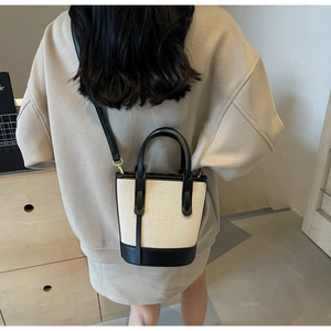 Detail of canvas bucket bag with black leather handle and gold hardware on model