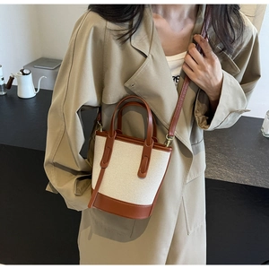 Detail of canvas and brown leather bucket bag styled with a khaki trench coat