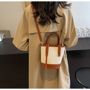 Chic beige canvas and brown leather bucket bag shown from behind on a model wearing a trench coat
