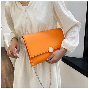 Borsa a busta arancione con catena dorata abbinata a un abito a pieghe color panna