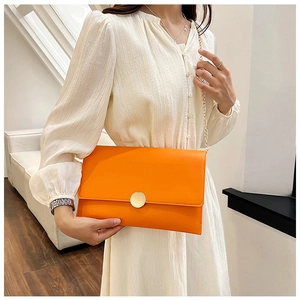 Borsa a busta arancione con catena e fibbia dorata su una modella in abito beige