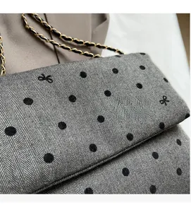 Detail of grey herringbone fabric with black polka dots and gold metal chain strap