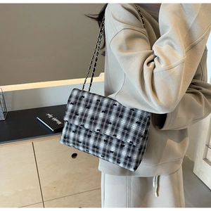 Detailed view of checkered shoulder bag with black bows and metal chain strap on model