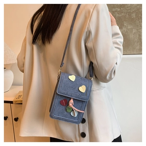 Blue denim mini crossbody bag with heart patches shown on model in white blazer
