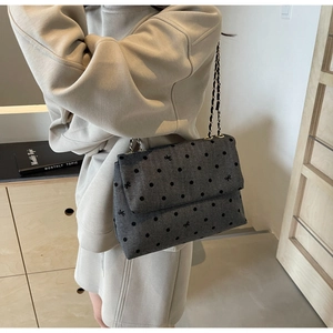 Detailed side view of a grey denim shoulder bag with black polka dots and chain strap