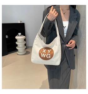 Close-up of beige canvas shoulder bag featuring a brown round leather patch with XY WG logo