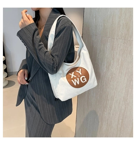Detail view of large canvas tote bag with brown XY WG patch on model in grey suit