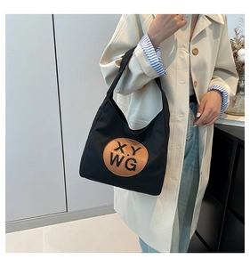 Detail of black canvas tote bag showing the round brown leather logo patch and texture