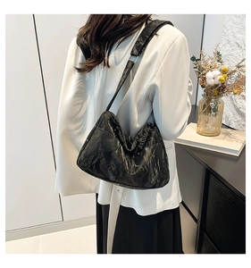 Detail of black pleated shoulder bag with wide strap and silver metal rings shown on model