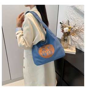 Blue canvas tote bag with embroidered logo patch shown on a beige trench coat