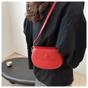 Detailed view of a red leather saddle crossbody bag worn by a model in a minimalist setting