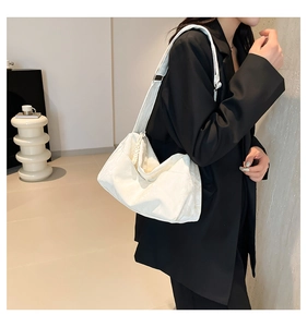 Detailed texture of white tote bag with embossed pattern worn by model in black suit