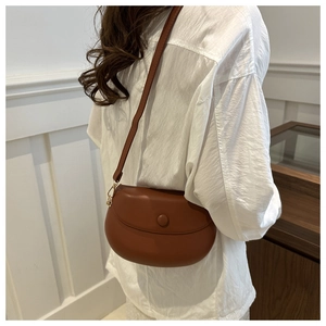 Brown faux leather saddle bag worn by a model with an adjustable shoulder strap