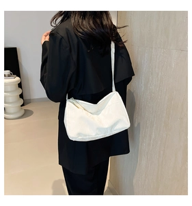 Detail view of white pleated nylon tote bag worn by model in black suit for minimalist style