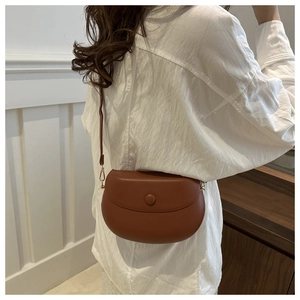 Detail of a deep brown matte leather saddle bag with round buckle and adjustable strap