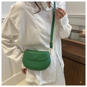 Detail of green leather saddle bag with gold metal hardware on casual white shirt