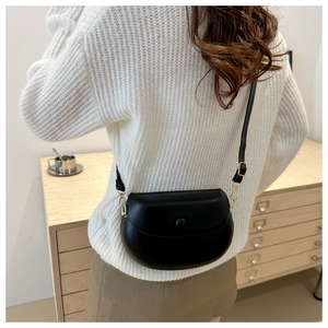 Detailed back view of a black leather saddle bag worn with a white knitted sweater