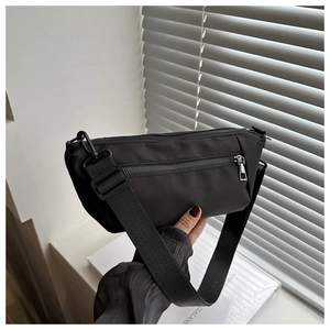 Detail of minimalist black nylon crossbody bag featuring adjustable wide strap and zipper
