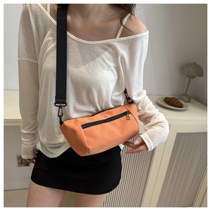 Detail of a bright orange crossbody bag with black zipper pockets and wide nylon strap
