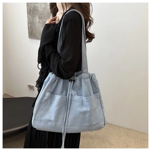 Detail of light blue denim tote bag with side drawstrings and front double pockets