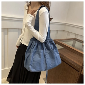 Detail view of the drawstring closure and front pockets on this blue denim tote bag