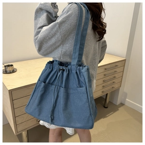 Detail of blue denim tote bag with drawstring closure and large front utility pockets