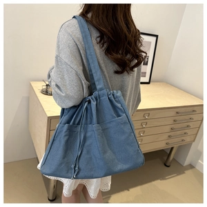 Detailed close-up of blue denim drawstring tote bag with outer pocket and shoulder strap