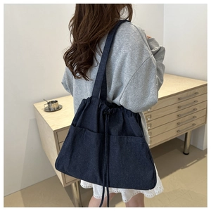 Detail of dark blue denim tote bag with dual front pockets and drawstring closure