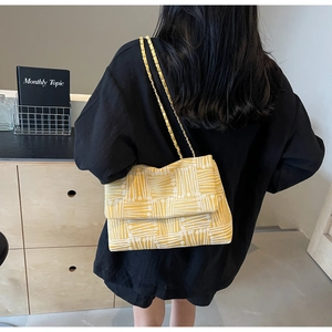 Detail of yellow and white jacquard fabric bag with golden metal chain strap on shoulder