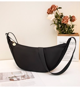 Detail of black crescent crossbody bag with golden metal zipper pull and wide strap