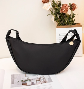 Close-up of a black crescent nylon crossbody bag with gold hardware on a wooden table