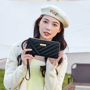 Women's long black quilted wallet with gold metal plate and wrist strap in an outdoor setting
