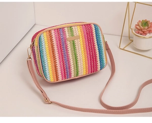 Detail of colorful striped straw bag with metallic plaque and pink leather shoulder strap