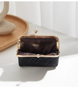 Detailed view of black woven shell coin purse with gold kiss-lock and brown lining