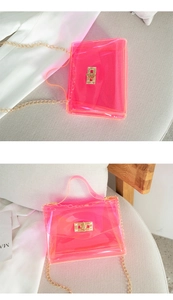 Macro shot of neon pink jelly bag with gold metal clasp and chain strap on light gray sofa