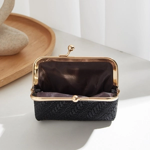 Elegant black woven shell coin purse with gold metal clasp on wooden display tray