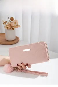 Detail of pink long wallet with wave stitching, double zippers and a fur ball pendant