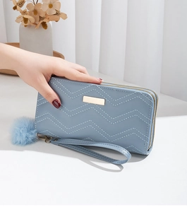 Detail of light blue quilted wallet with dual zippers and a soft fur ball keychain