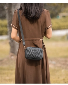 Rear view of a black quilted camera bag with heart embroidery and wide canvas strap