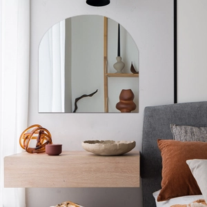 Frameless arched wall mirror in modern bedroom setting with warm natural lighting