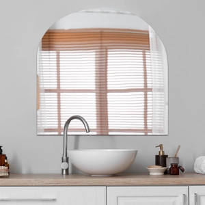 Modern arch-shaped frameless wall mirror reflecting light in a clean bathroom interior