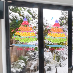 Colorful hand-drawn Christmas tree window decals on glass with snowy garden background