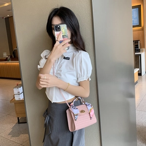 Pink croc-embossed mini handbag with silk scarf and gold buckle in lifestyle setting