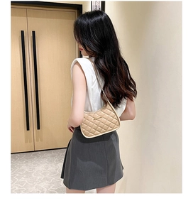 Side view of model wearing a beige quilted hobo bag with gold logo and leather strap